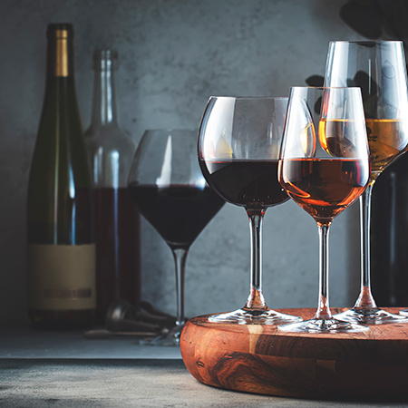 A collection of wine glasses in the foreground with two bottles of wine in the background.